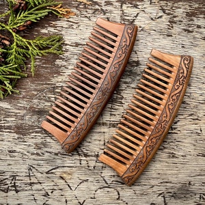 May include: Two wooden combs with intricate carved designs. The combs are brown and have a curved shape. They are lying on a wooden surface.