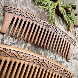 May include: Two wooden combs with intricate carved designs on the handle. The combs are brown and have a natural wood finish.