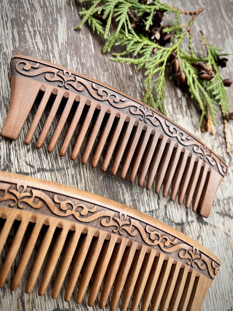 May include: Two wooden combs with intricate carved designs on the handle. The combs are brown and have a natural wood finish.