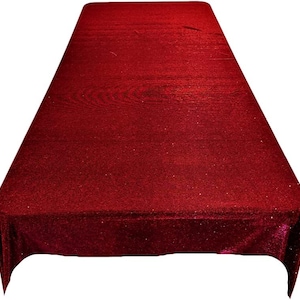 May include: A red sparkly tablecloth with a smooth, shiny surface. The tablecloth is rectangular and has a slight sheen.
