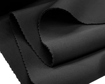 Puede incluir: Una pieza de tela negra sólida con una textura de superficie lisa y mate. El material está doblado en capas, mostrando un borde limpio y acabado con un sutil patrón de corte en zigzag o dentado a lo largo del lado del material textil.