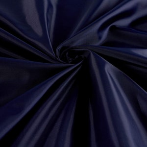 May include: A close-up of a deep blue fabric with a smooth, silky texture. The fabric is folded and draped, creating soft, flowing lines.