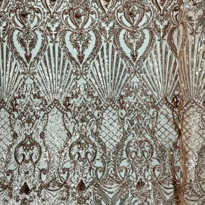 May include: Rose gold sequined fabric with a damask pattern. The fabric has a delicate, intricate design with a shimmering finish.