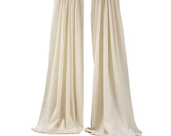May include: A pair of off-white curtains hanging from a black curtain rod. The curtains are made of a soft, flowing fabric.