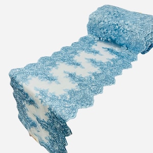 May include: A roll of light blue lace fabric with a floral pattern. The lace is intricately detailed with a scalloped edge, and the fabric is partially unrolled, revealing its delicate design. Ideal for crafting or decorating.