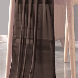 May include: A brown table runner draped over a light-colored wooden table. The runner is made of a sheer fabric, creating soft folds. The table has four legs and is set against a neutral background.
