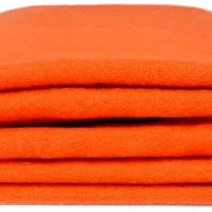 Puede incluir: Una manta de forro polar de color naranja brillante doblada en tres. La manta es suave y cálida, perfecta para mantenerte abrigado en un día frío.