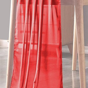Puede incluir: Un camino de mesa rojo brillante hecho de una tela suave y fluida. El camino de mesa está drapeado sobre una mesa de madera y cuelga hasta el suelo.