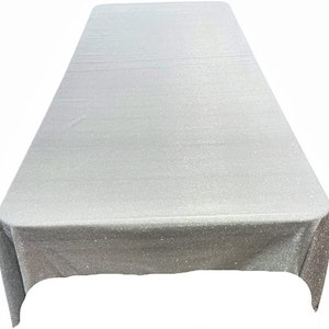 May include: A silver glitter tablecloth with a rectangular shape. The tablecloth has a subtle shimmer and is perfect for adding a touch of sparkle to any table setting.