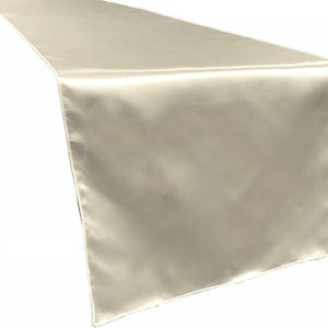 May include: A cream-colored satin table runner. The runner is smooth and has a subtle sheen.