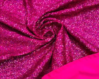 May include: A close-up of a pink fabric with sequins. The fabric is folded and the sequins are catching the light.