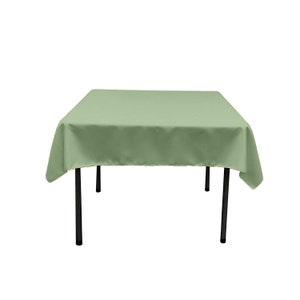 May include: A square green tablecloth draped over a table with black legs.