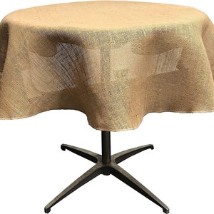 May include: A round, brown burlap tablecloth with a slightly ruffled edge. The tablecloth is draped over a round table with a black metal base.