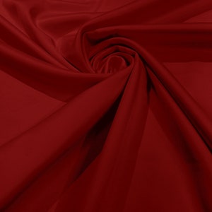 May include: A close-up of a deep red fabric with a smooth, silky texture. The fabric is draped and folded, creating soft, flowing lines.