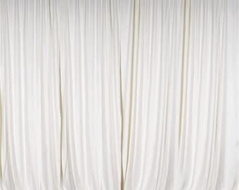 May include: A white backdrop made of fabric with a smooth, wrinkle-free finish. The backdrop is hung from a ceiling track and is ideal for photography or video backdrops.