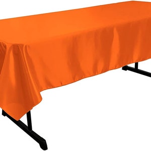 以下が含まれることがあります： テーブルにかけられた明るいオレンジ色の長方形のテーブルクロス。テーブルクロスは滑らかでサテンのような生地で作られています。