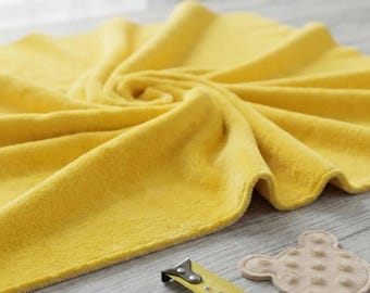 Puede incluir: Una manta de felpa de color amarillo brillante con una superficie suave y texturizada dispuesta en un patrón de remolino circular. Se ve una cinta métrica amarilla que muestra 145 a 147 cm, junto a una pieza de tela beige, circular y texturizada.