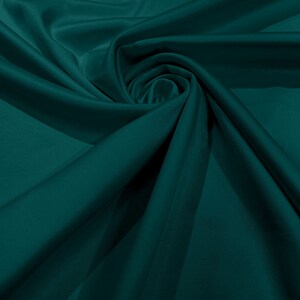 Può includere: Un tessuto color verde ottanio scuro a tinta unita con una consistenza liscia e opaca. Il materiale è disposto in una serie di pieghe morbide e fluide e drappeggi profondi che creano un motivo dinamico di luci e ombre sulla superficie.