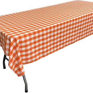 May include: Orange and white checkered tablecloth with a white border. The tablecloth is draped over a table with metal legs.