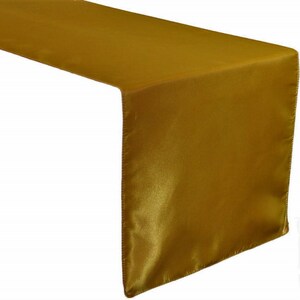 May include: A gold satin table runner. The runner is a rectangular shape and has a smooth, silky texture.