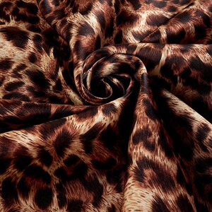 May include: Close-up of a brown and cream leopard print fabric with a silky texture. The fabric is folded and draped, creating a swirling pattern.