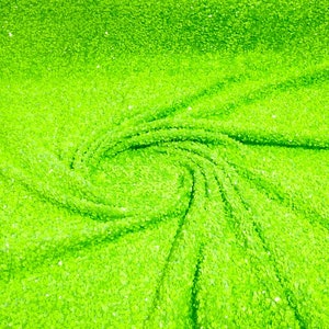 Puede incluir: Primer plano de una tela verde brillante con una superficie texturizada y brillante. La tela está doblada y drapeada en un patrón de remolino.