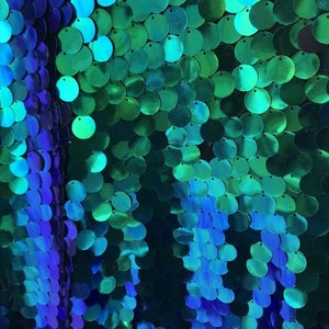 May include: A close-up of iridescent blue and green sequins arranged in a gradient pattern. The sequins are round and have a metallic sheen.