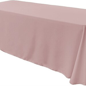 Puede incluir: Un mantel rectangular de color rosa polvoriento con un acabado liso y sin arrugas. El mantel tiene un caída de 15 pulgadas (38 cm) en todos los lados.