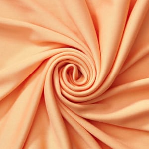 May include: Close-up of peach-colored fabric with a swirling pattern. The fabric appears soft and has a slight sheen, with folds and shadows creating depth. The color is a warm, inviting tone.