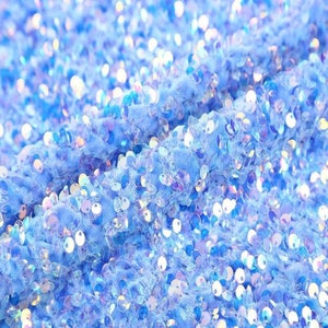 Può includere: Primo piano di un tessuto blu chiaro ricoperto di paillettes iridescenti. Le paillettes sono disposte in modo casuale e creano un effetto scintillante.