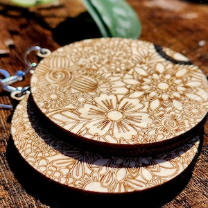 May include: A pair of wooden earrings with a floral design. The earrings are round and have a delicate, intricate pattern.
