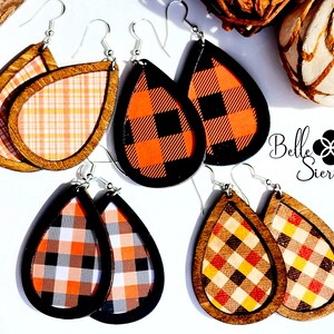 May include: Three pairs of teardrop-shaped earrings with a wooden frame and a plaid pattern. The patterns include orange, black, white, and yellow plaid. The earrings are labeled "Belle Sierra".