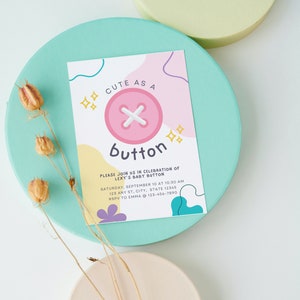 Może przedstawiać: Zaproszenie na baby shower z różowym guzikiem i tekstem "Cute as a button" i "Lexy's Baby Button". Zaproszenie zawiera datę, godzinę i miejsce wydarzenia, a także informacje o RSVP.