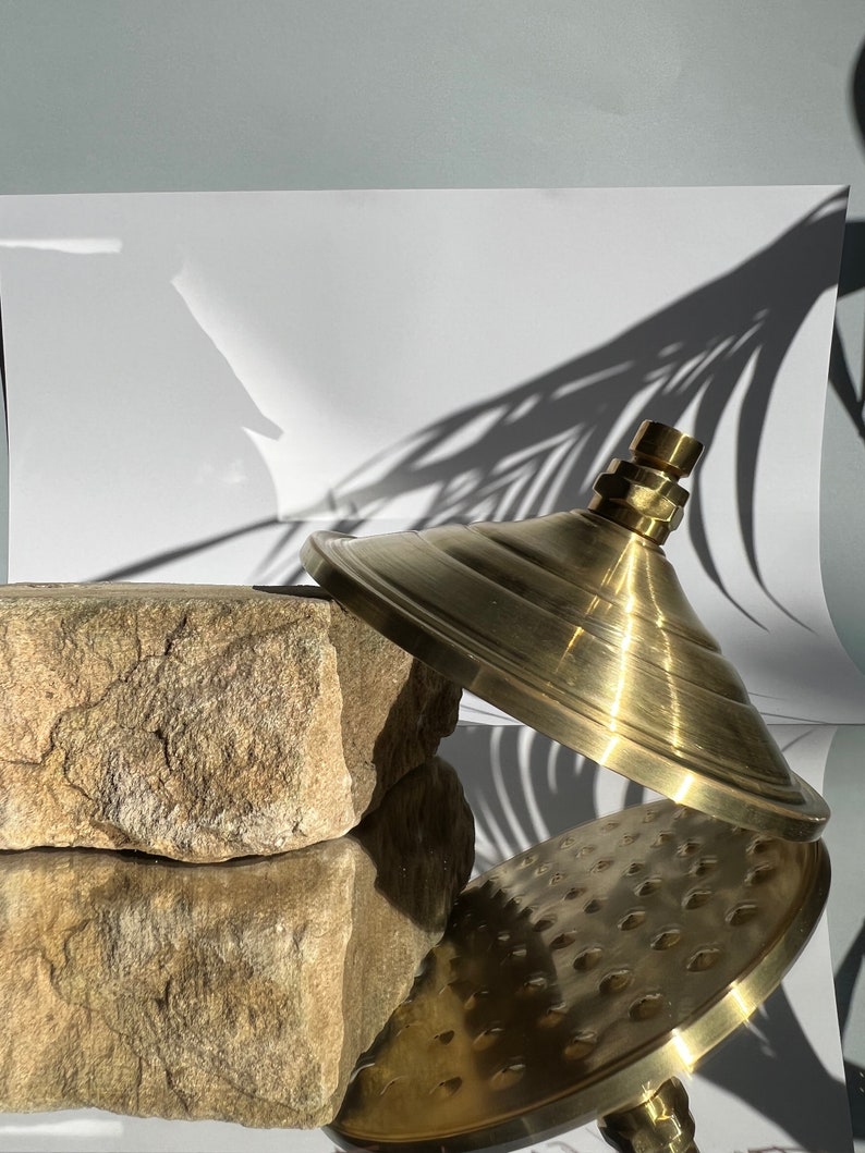 Puede incluir: Un cabezal de ducha dorado con una base redonda y plana y una parte superior abovedada. El cabezal de ducha est&aacute; sobre una roca marr&oacute;n y rugosa.