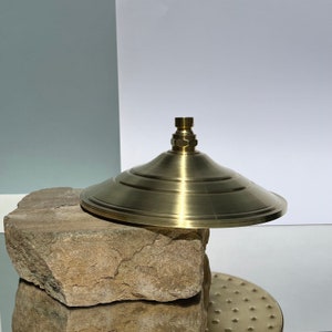 Puede incluir: Un cabezal de ducha de color dorado con un dise&ntilde;o redondo y plano. El cabezal de ducha est&aacute; colocado sobre una roca marr&oacute;n.