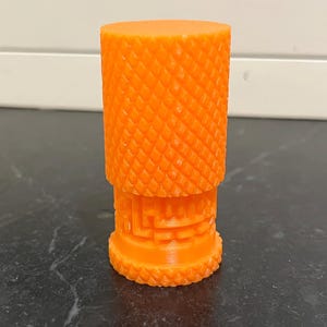 May include: Orange plastic 3D printed object with a textured surface and a maze pattern.