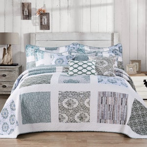 May include: A bedspread and pillow set in a patchwork design, featuring squares of blue, green, and white patterns. The quilt has floral and geometric designs. The bed is made up with decorative pillows and a white headboard.