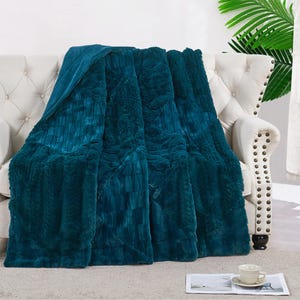 May include: A teal blue faux fur throw blanket with a quilted pattern. The blanket is draped over a white couch.
