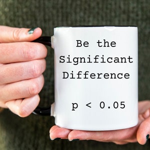 Puede incluir: Taza de cerámica blanca con asa negra. La taza tiene texto negro que dice "Be the Significant Difference p < 0.05".