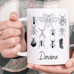May include: White ceramic mug with a black and white illustration of ants and a bee. The mug has the name "Davina" written on the bottom.