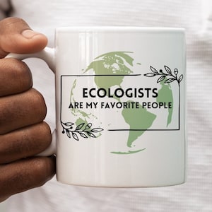 Può includere: Tazza in ceramica bianca con un'illustrazione verde e nera della Terra e il testo "Gli ecologisti sono le mie persone preferite".