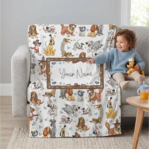 May include: A white blanket featuring a repeating pattern of cartoon dogs in various poses. The blanket has a brown border with the words "Your Name" in the center. The blanket is draped over a gray couch.