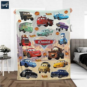 Puede incluir: Una manta suave de color beige con varios personajes de coches de dibujos animados de la película Cars. La manta incluye el nombre "David" en un emblema rojo y blanco. Los coches son de varios colores, incluyendo rojo, azul, verde y amarillo.
