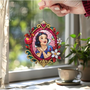 May include: A stained glass window decoration featuring Snow White in a decorative frame. The frame is gold with red, pink, and green accents. The image is held by a silver chain.