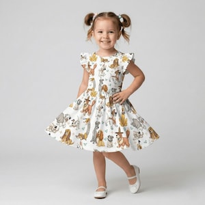 May include: A white dress with a playful dog print. The dress features a flared skirt and ruffled sleeves. The print includes various dog breeds in shades of brown, gray, and yellow. The dress is worn with white shoes.