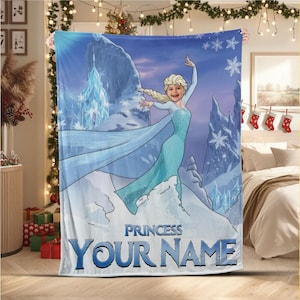 Op de afbeelding: Een blauw-witte fleece deken met een cartoonprinses in een blauwe jurk, tegen een besneeuwde bergachtergrond. De deken heeft de tekst "PRINCESS YOUR NAME" in het blauw.