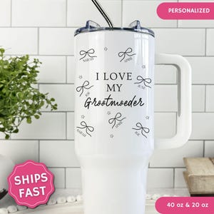 May include: A white stainless steel tumbler with a handle and a straw, featuring the black text I LOVE MY Grootmoeder, surrounded by black line-art bows and small stars. The names Sarah, April, and Joe are printed below individual bows.