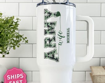 May include: A white stainless steel tumbler with a handle and a straw, featuring the word ARMY in a green camouflage pattern, the script text wife, a small green heart, and the name MICHEAL printed vertically in green on the side.
