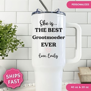 May include: A white stainless steel tumbler with a handle and a straw, featuring the black printed text "She is... THE BEST Grootmoeder EVER" with a small pink heart and the text "love, Emily" below it. The tumbler is available in 40 oz and 20 oz.