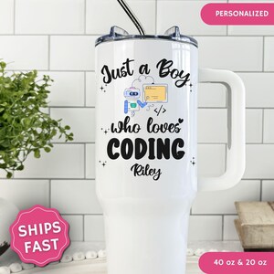 May include: A white stainless steel tumbler with a handle and a straw, featuring the black text Just a Boy who loves CODING, a small blue robot graphic, a yellow computer screen icon, and the name Riley printed in a script font on the front.